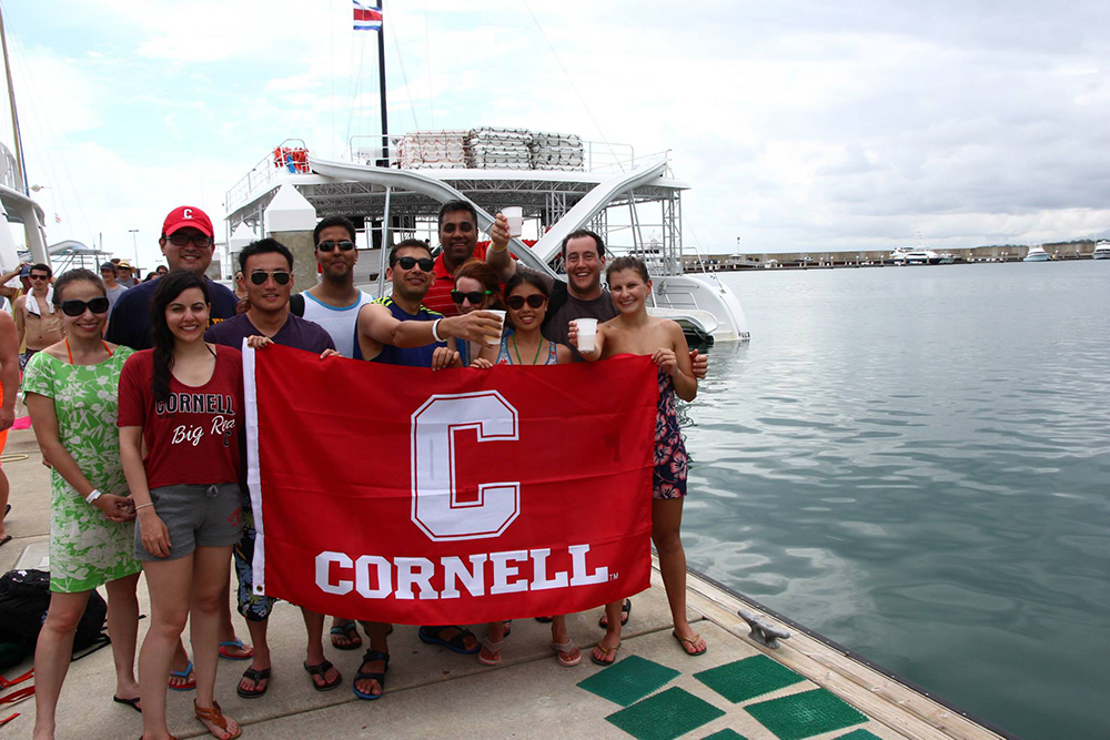 Cornell MBA students with a Cornell flag next to a boat